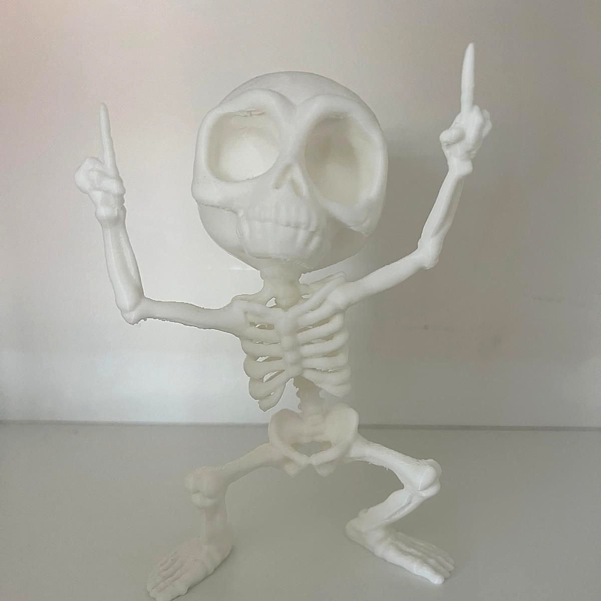 A white 3D-printed skeleton with a big skull, both arms pointing up and knees bent in a dance pose