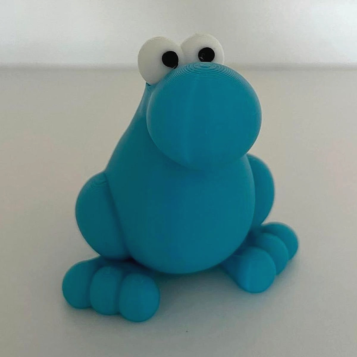 A bright blue 3D-printed critter with big white googly eyes, a round nose and stubby toes