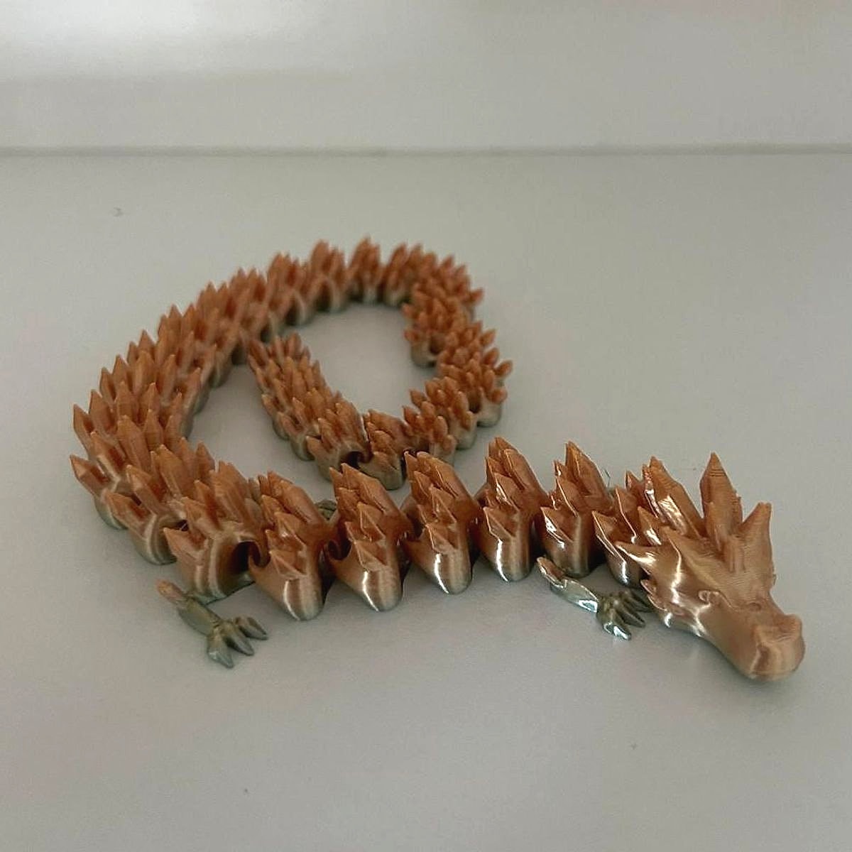 A copper and gold articulated dragon curled in loops on a white shelf