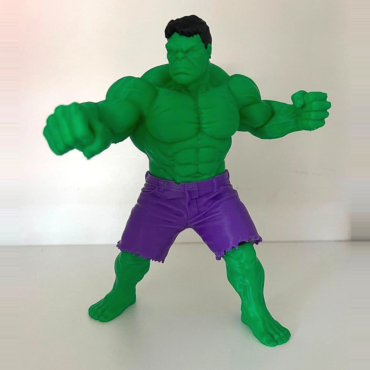 A green 3D-printed muscular figure in torn purple shorts with both fists forward