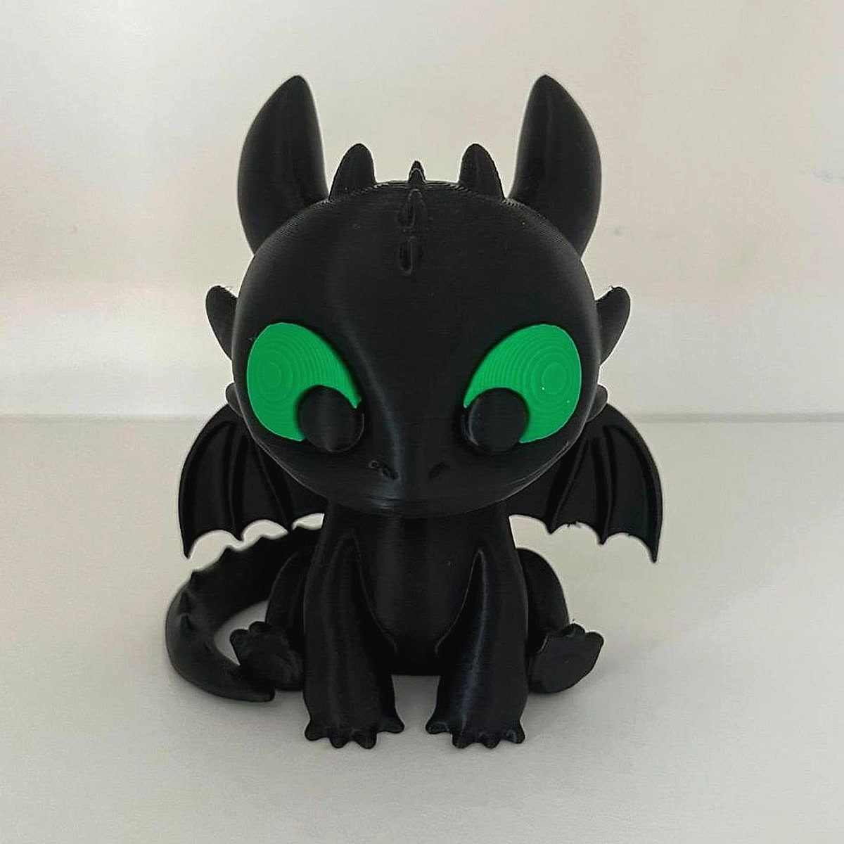 A black 3D-printed baby dragon with big green eyes, small wings and a curled tail